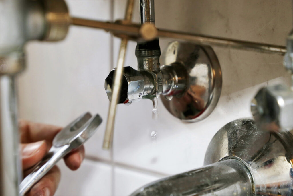A person using a wrench to fix a leak under a sink
