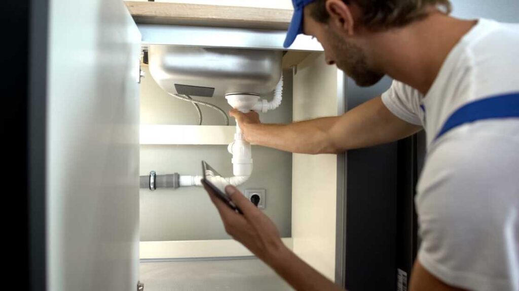 Plumber inspecting pipes under sink