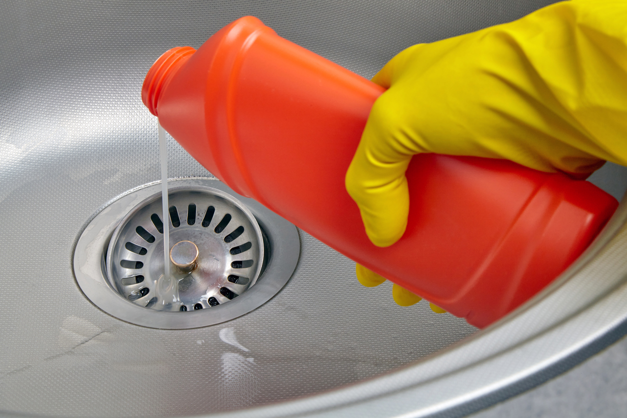 Hand in yellow rubber glove pour sewer pipe cleaner down the kitchen sink drain