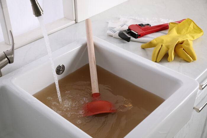 Clogged kitchen sink with plunger sitting in dirty water